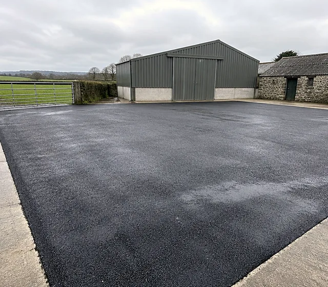 A tarmacadam farm yard in front of farm sheds