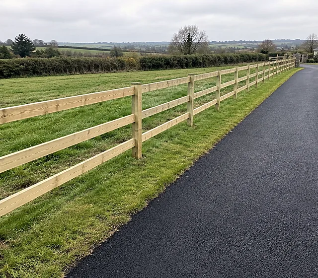 A timber post and rail fence beside a tarmacadam driveway