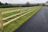 A timber post and rail fence beside a tarmacadam driveway