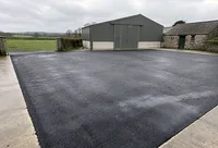 A tarmacadam farm yard in front of farm sheds