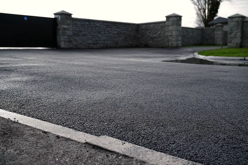 Tarmacadam meeting a granite kerb at a gated entrance